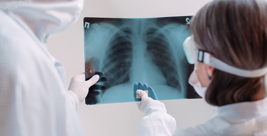 two clinicians in white coats and masks examine X-ray image