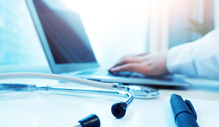 Close-up of a laptop, stethoscope, and physician’s forearm in white coat